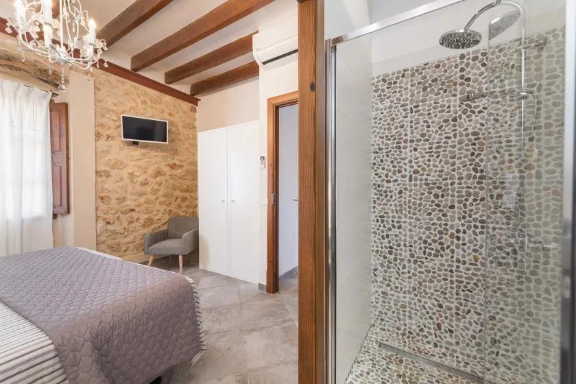 Un dormitorio con una cama, una pared de piedra y una ducha con mampara de vidrio.