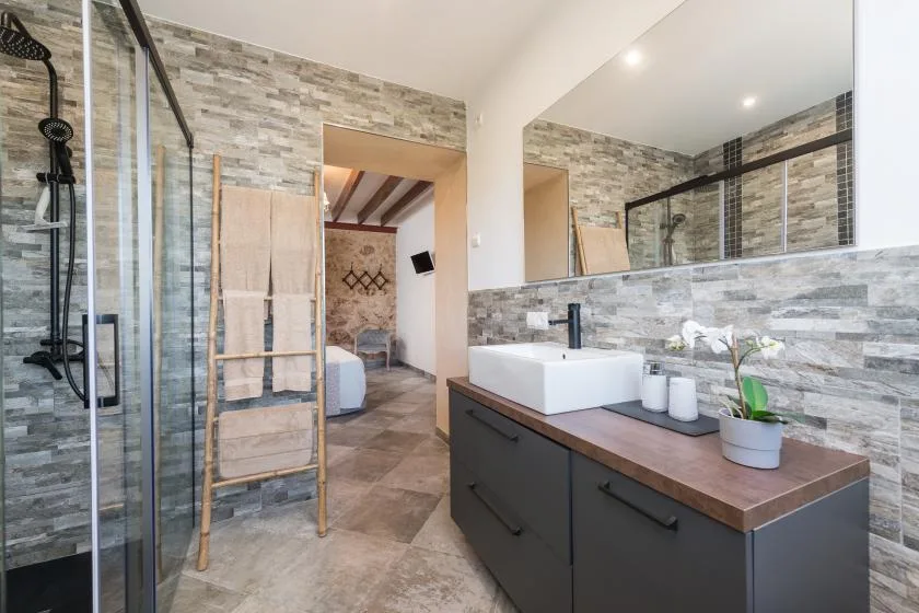 Un baño con un mueble largo, lavabo sobre encimera y ducha con mampara de vidrio.