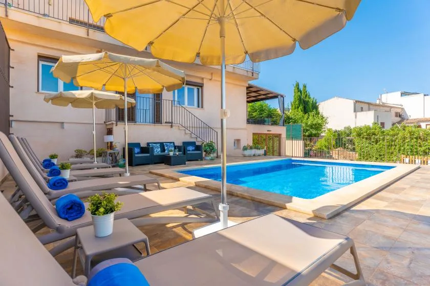 Zona de piscina al aire libre con asientos reclinables y sombrillas amarillas.