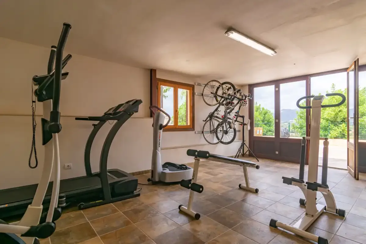 Un gimnasio con equipo de ejercicio y bicicletas junto a grandes puertas de vidrio.