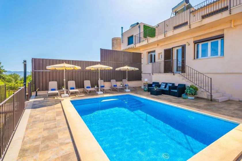 Una piscina al aire libre junto a una terraza con tumbonas y sombrillas.