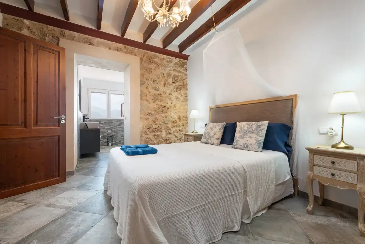 Un dormitorio con una cama bien tendida y vigas expuestas en el techo.