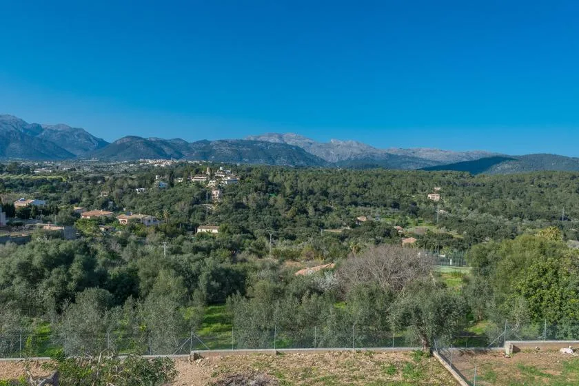 Un paisaje rural con casas dispersas y una cordillera a lo lejos.