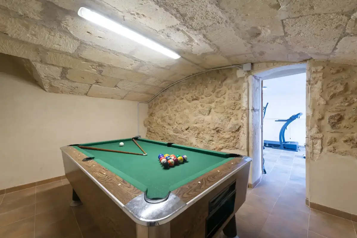 Sala de billar con una mesa verde bajo un techo de piedra.