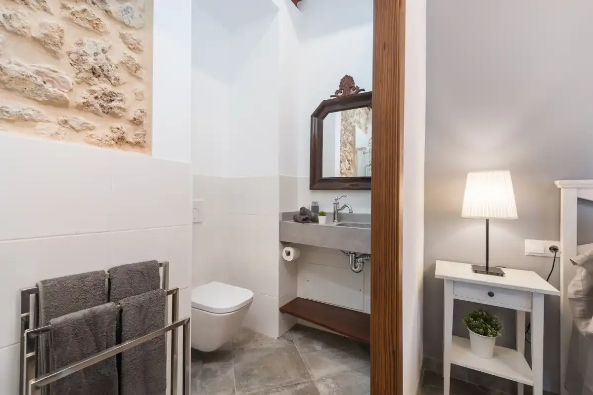 Un baño con inodoro, lavabo y una mesita con una lámpara encendida.