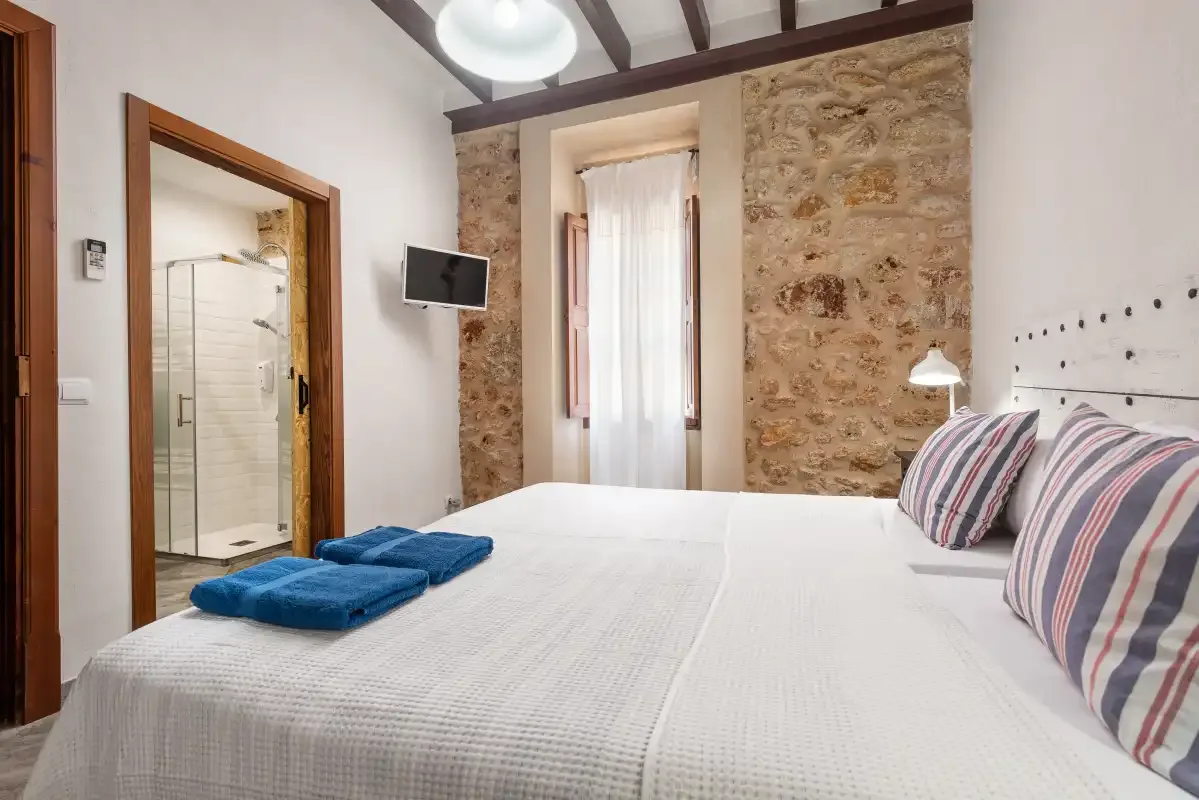 Un dormitorio con una cama tendida, almohadas a rayas y una pared de piedra vista.