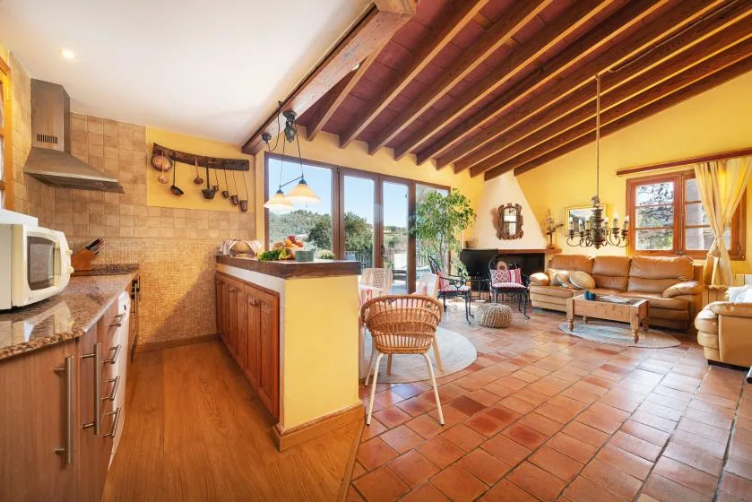 An open-plan kitchen and living area with wood-beamed ceiling and tiled floor.