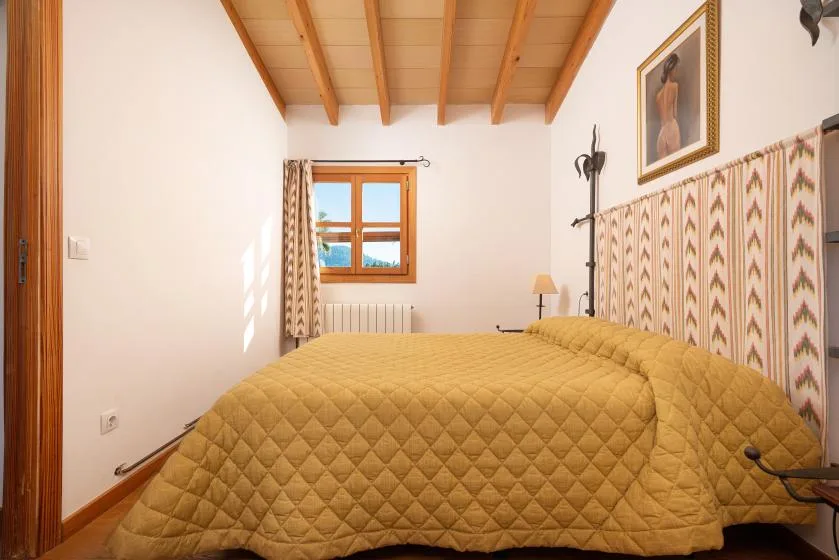 A bedroom with a large bed, patterned wall covering, and a wood-framed window.