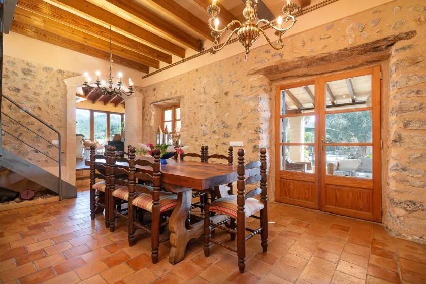 A rustic dining room with a long wooden table beneath exposed ceiling beams.
