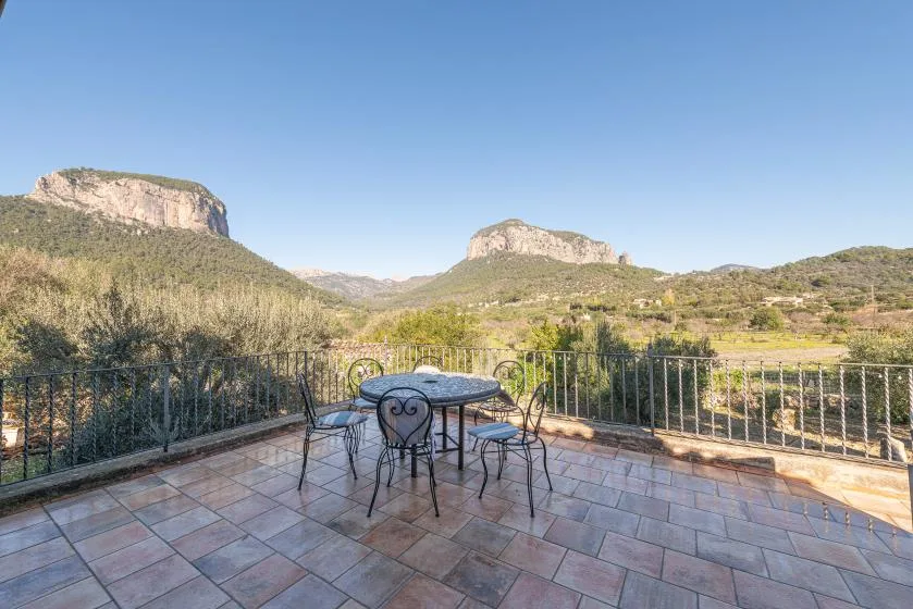 A tiled terrace with outdoor seating overlooks a green mountain valley.