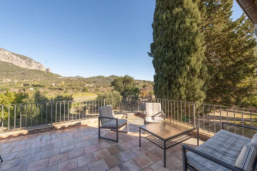 A tiled terrace with outdoor seating overlooks a green valley and distant hills.