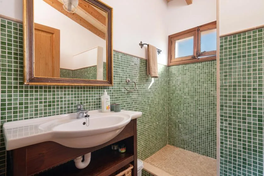 A bathroom with a sink, green tiled walls, and a shower area.