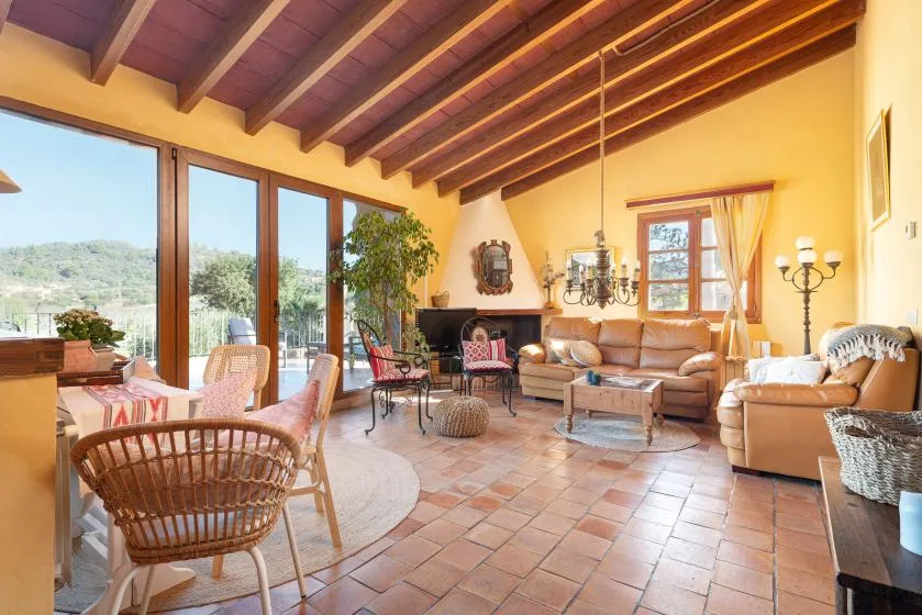 A bright living room with seating, a fireplace, and large windows overlooking greenery.