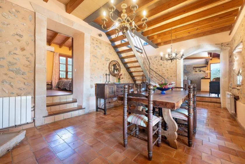 A dining room with a wooden table beneath exposed ceiling beams and a staircase.