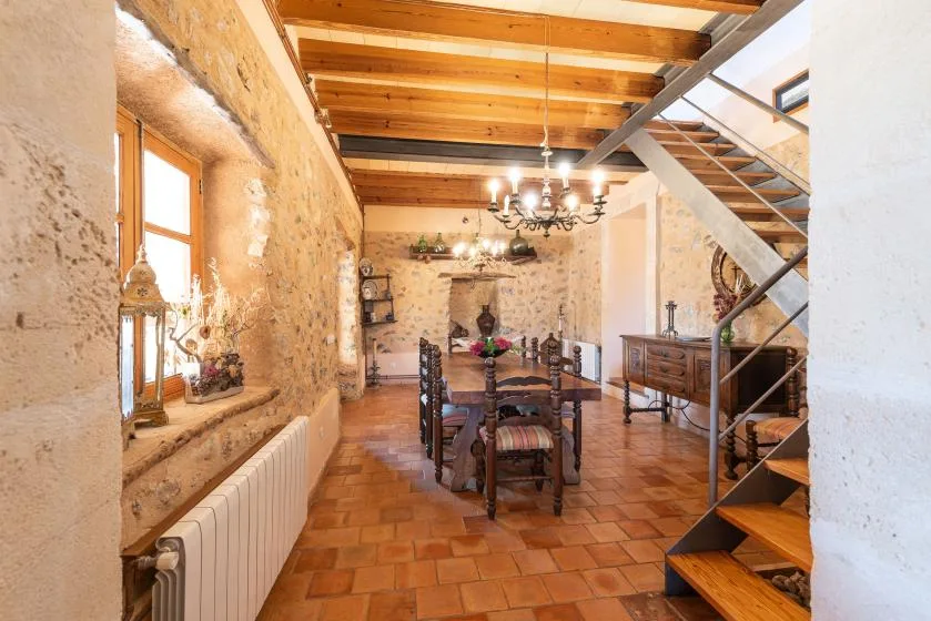 A rustic dining room with a long wooden table beneath exposed ceiling beams.