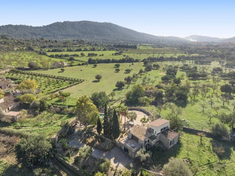 Aerial view of a rural stone house surrounded by green fields and hills.