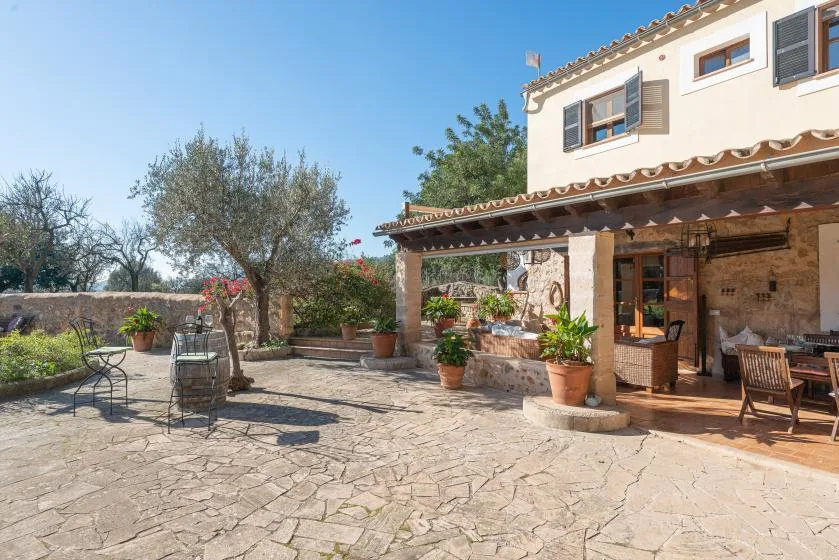 A stone-paved outdoor patio beside a house, with potted plants and seating.