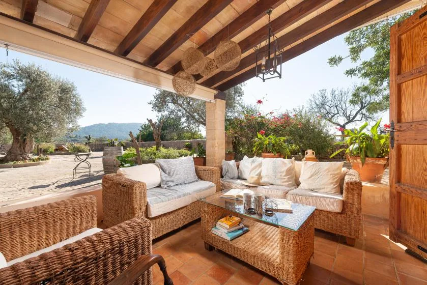 A covered outdoor patio has wicker seating, a low table, and garden views.