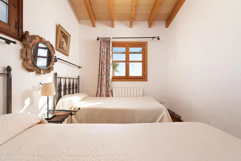 A bright bedroom with two beds and a window beneath exposed wooden beams.