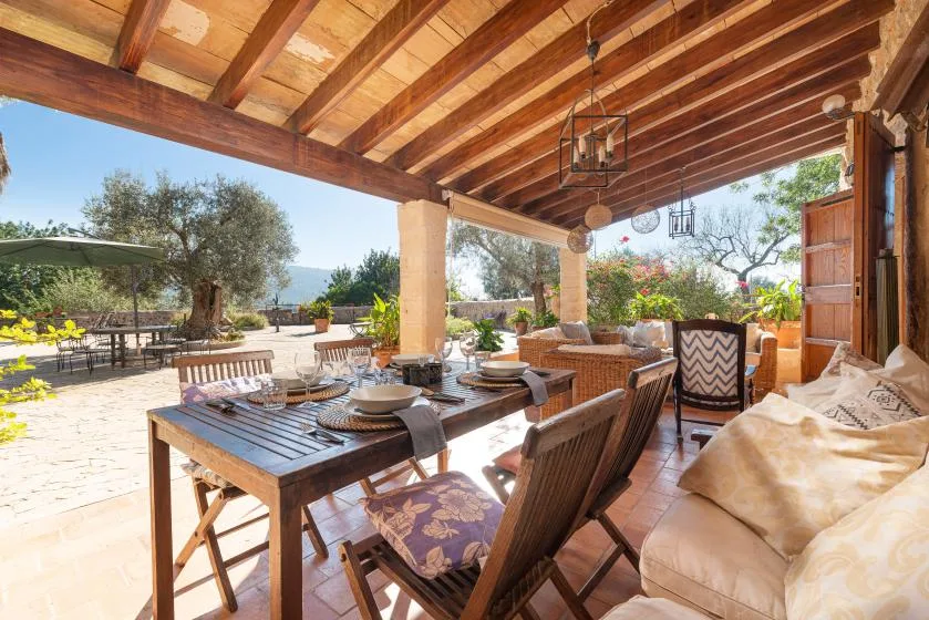 A covered outdoor dining area with a long table and cushioned seating.