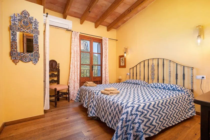 A bedroom with a patterned bedspread, a window, and exposed wooden ceiling beams.
