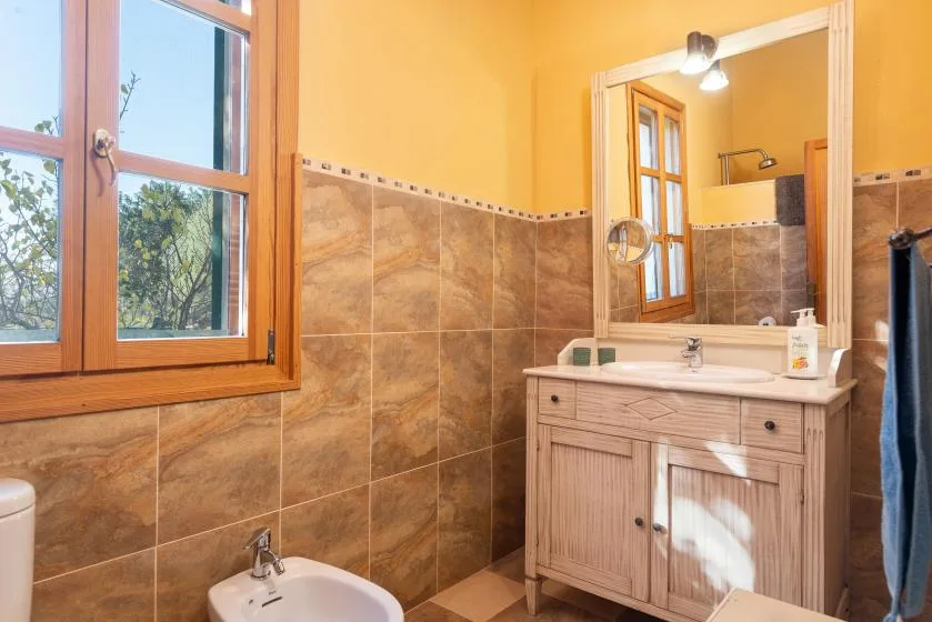 A tiled bathroom with a sink vanity and a large wooden-framed window.