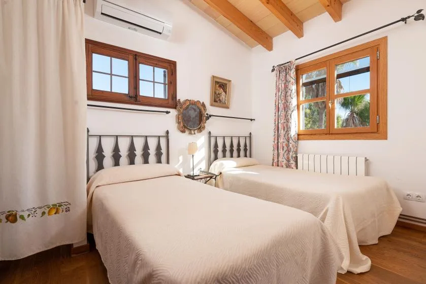 A bedroom with two beds, wooden-framed windows, and exposed ceiling beams.