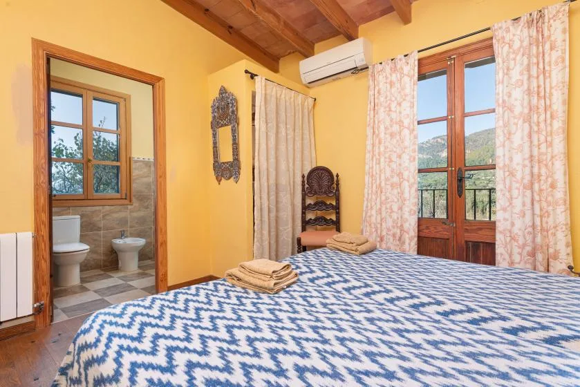 A bedroom with patterned bedding, a wooden balcony door, and a bathroom visible through the doorway.