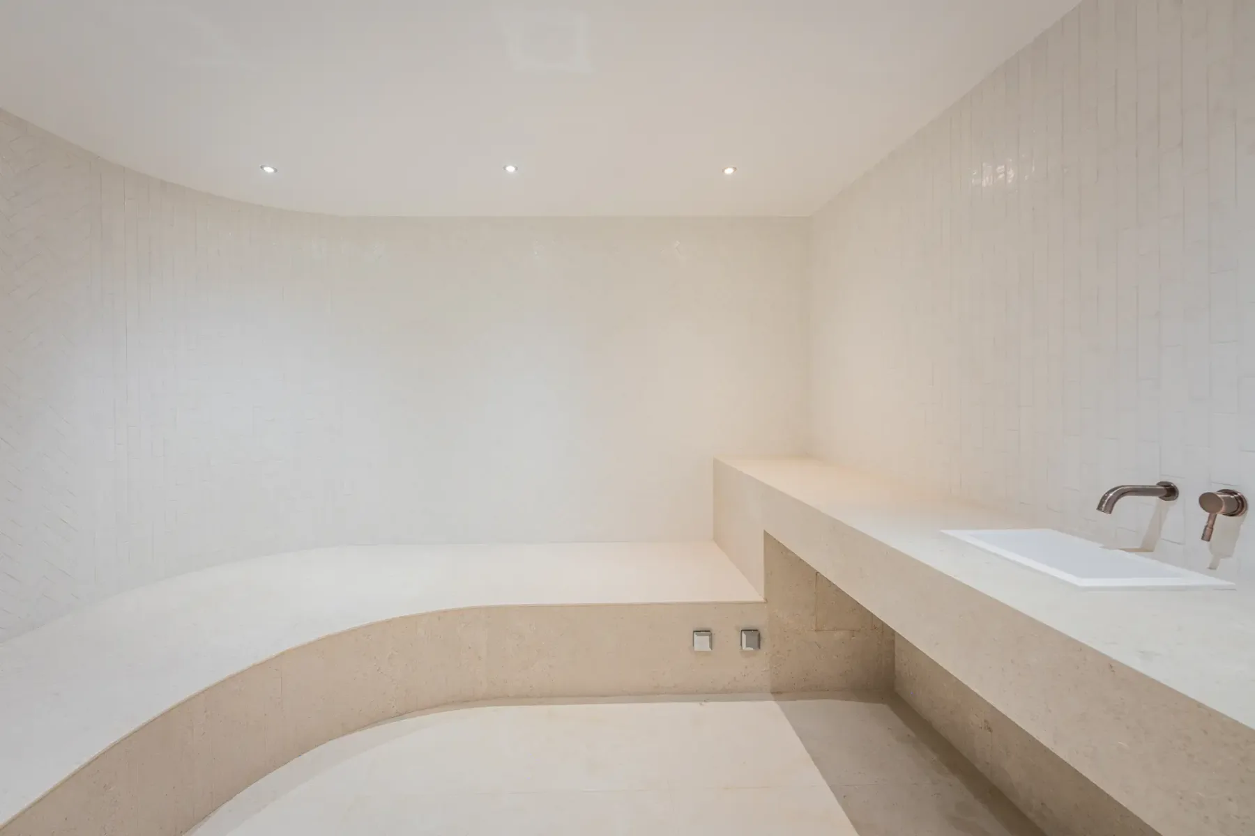 Baño de vapor con azulejos, banco integrado y lavabo con grifo.