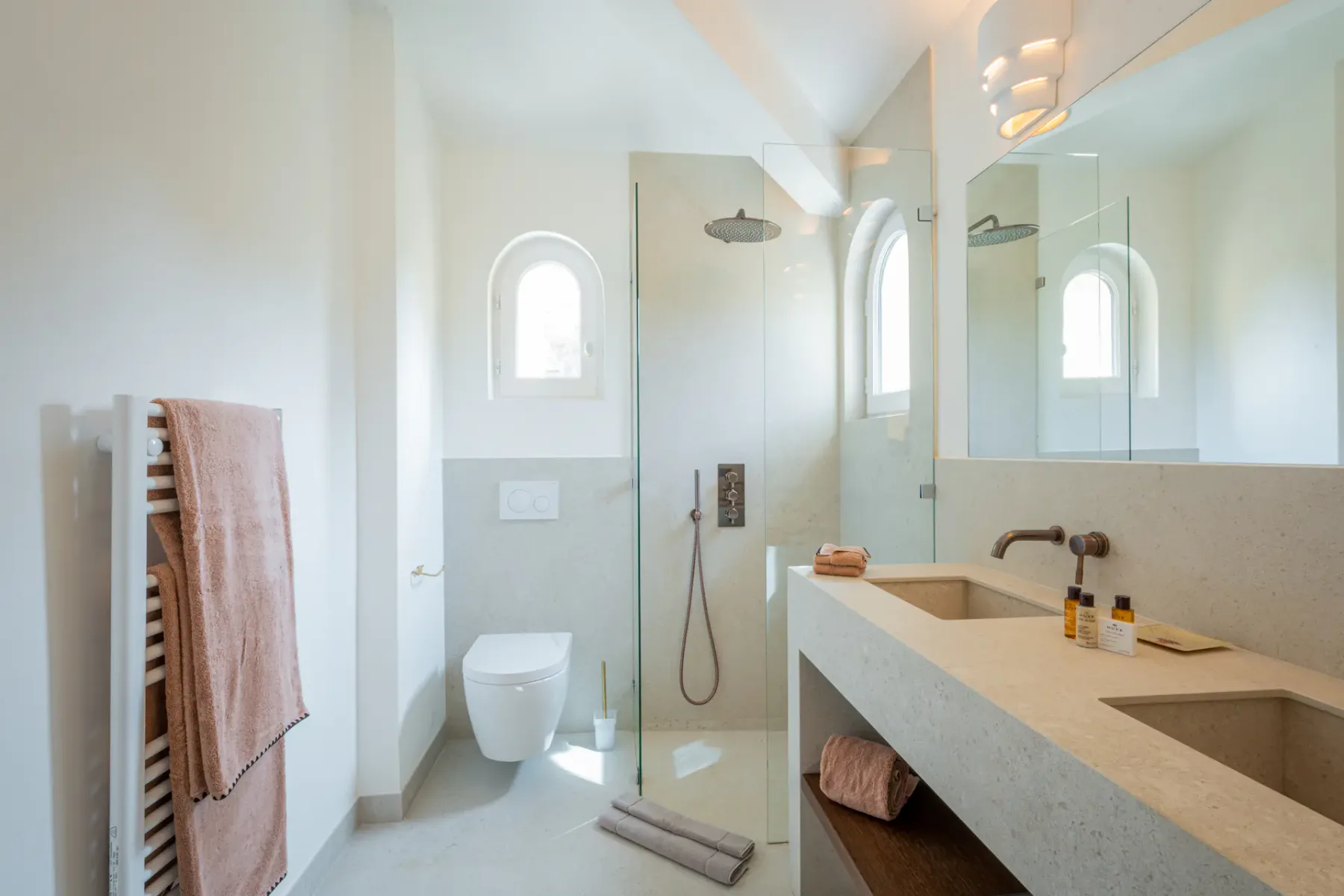 Baño luminoso con ducha y una encimera larga con lavabos.
