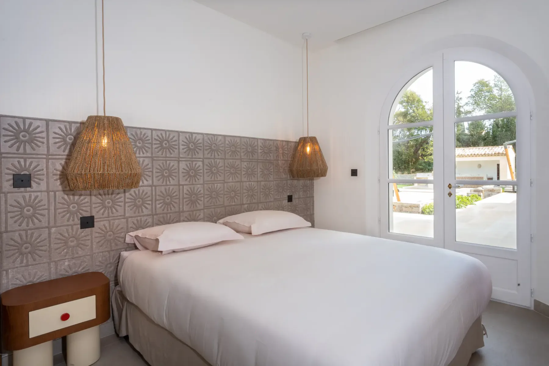 Dormitorio con cama doble, lámparas colgantes junto a la cama y una puerta doble que da a una terraza exterior.