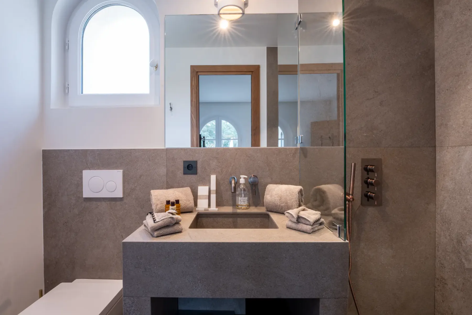 Baño con lavabo, espejo y luz natural procedente de una ventana situada sobre el inodoro