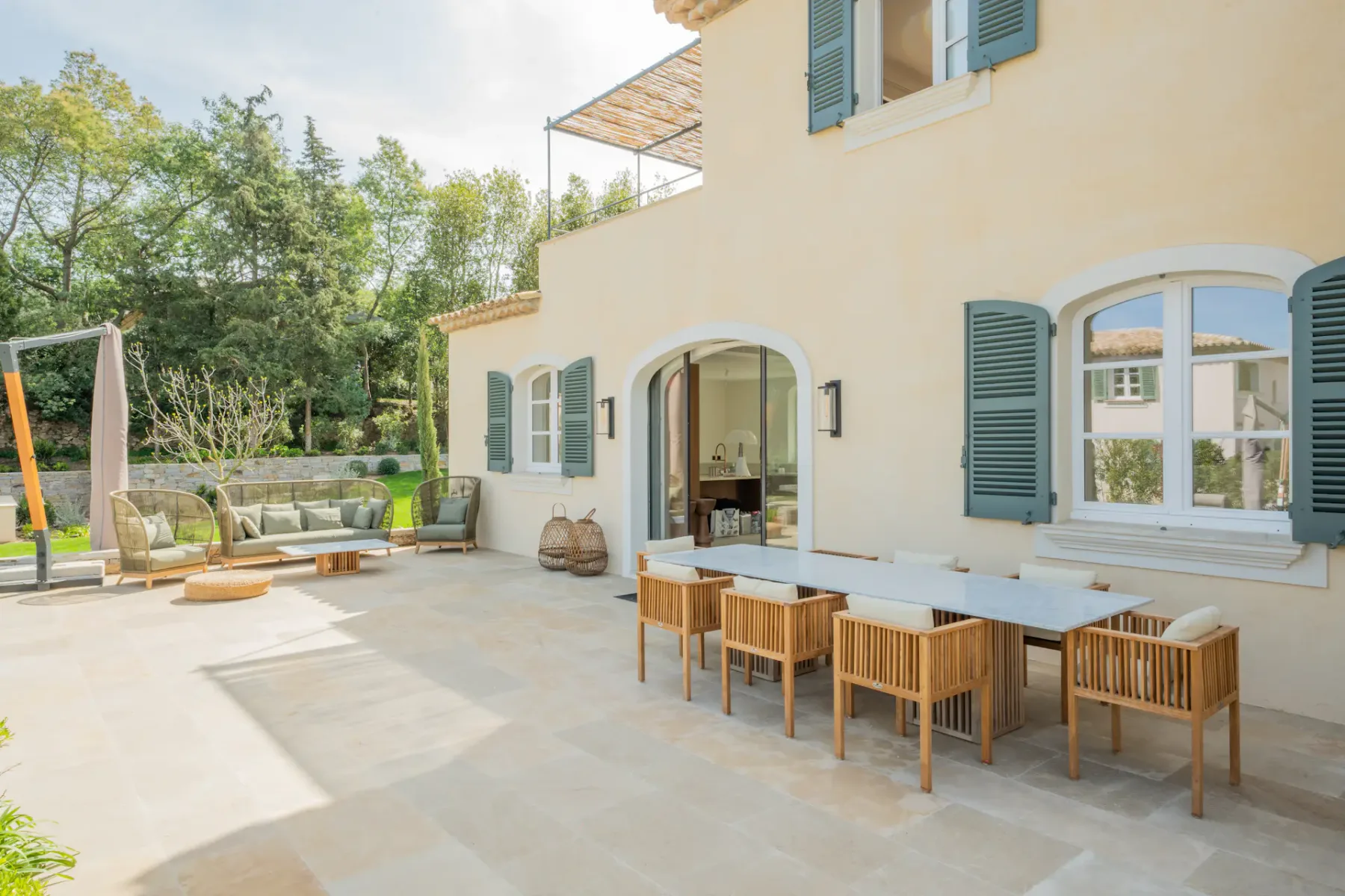 Un patio pavimentado junto a una casa clara, con una mesa de comedor exterior y asientos.