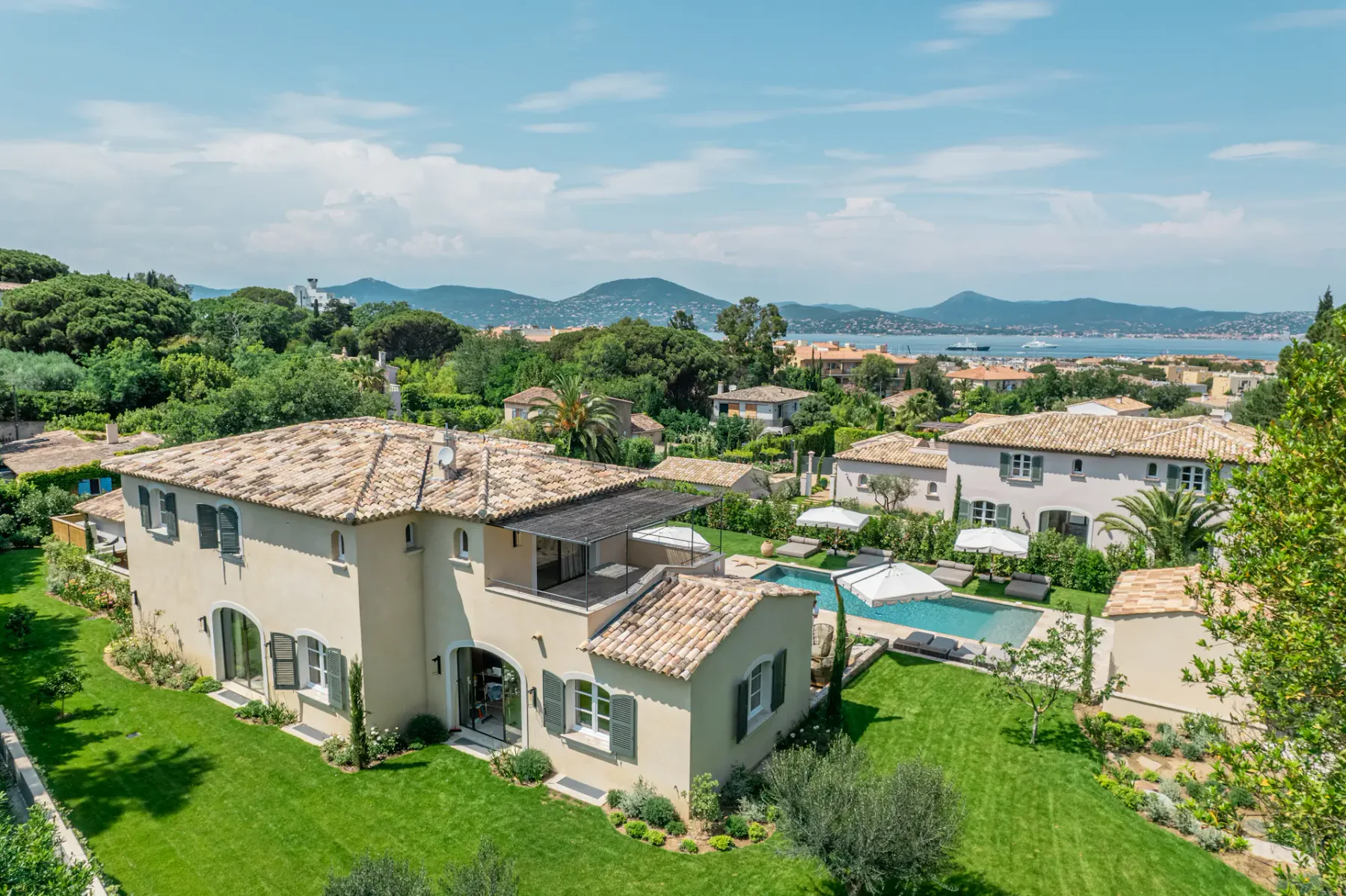 Una villa moderna y un jardín bien cuidado con piscina, con vistas al mar a lo lejos.
