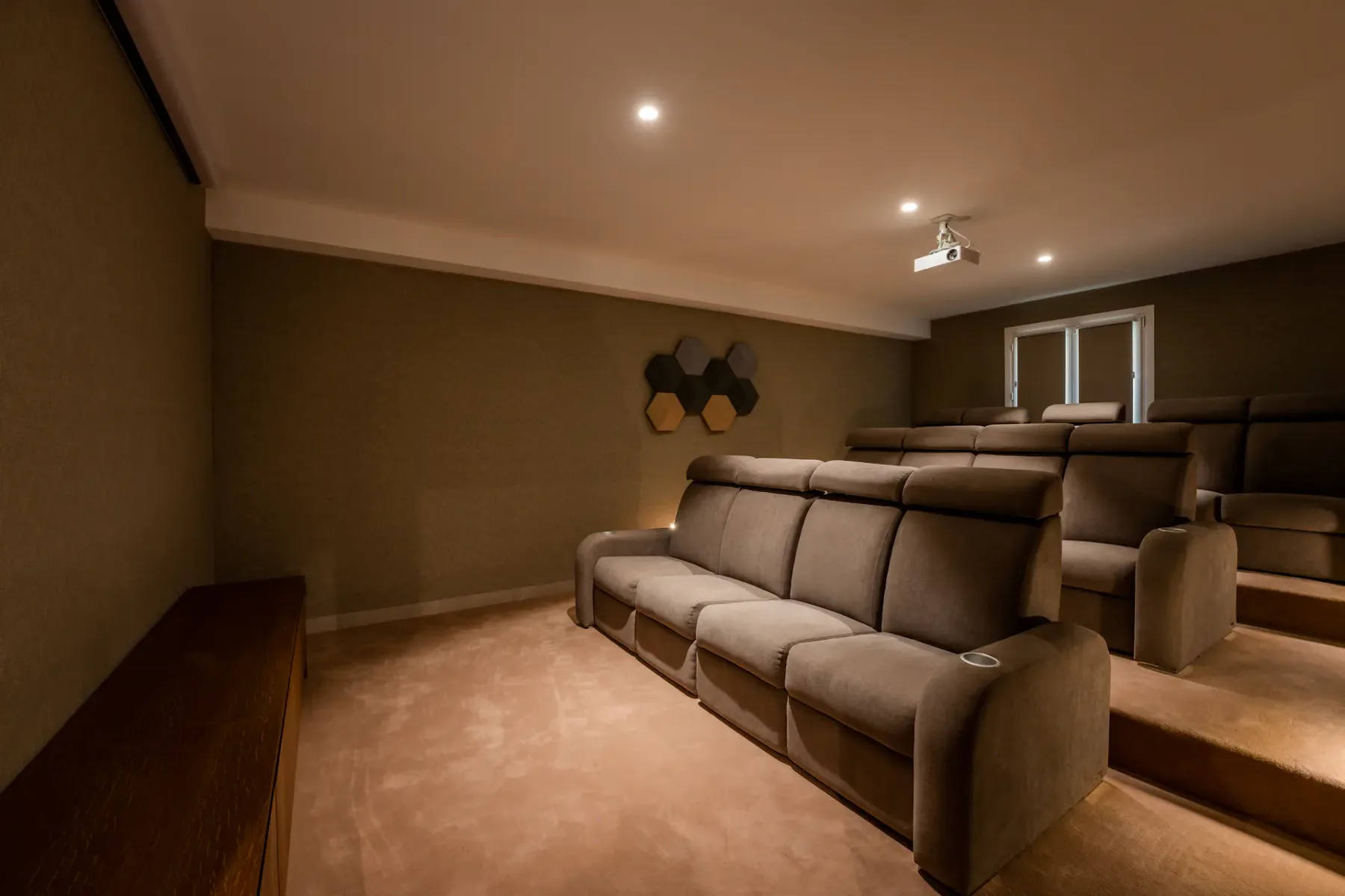 Un cine en casa con filas escalonadas de asientos tapizados y un proyector en el techo.