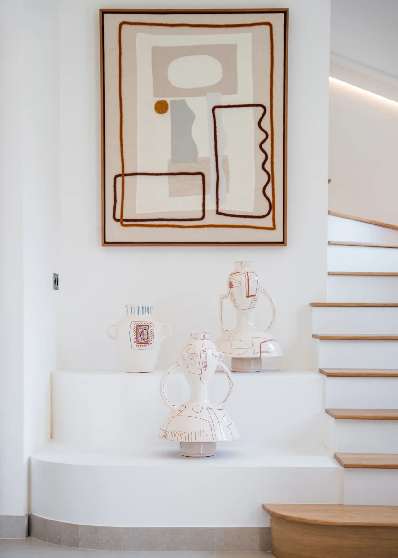 Una pintura abstracta enmarcada cuelga sobre vasijas decorativas de cerámica junto a una escalera.