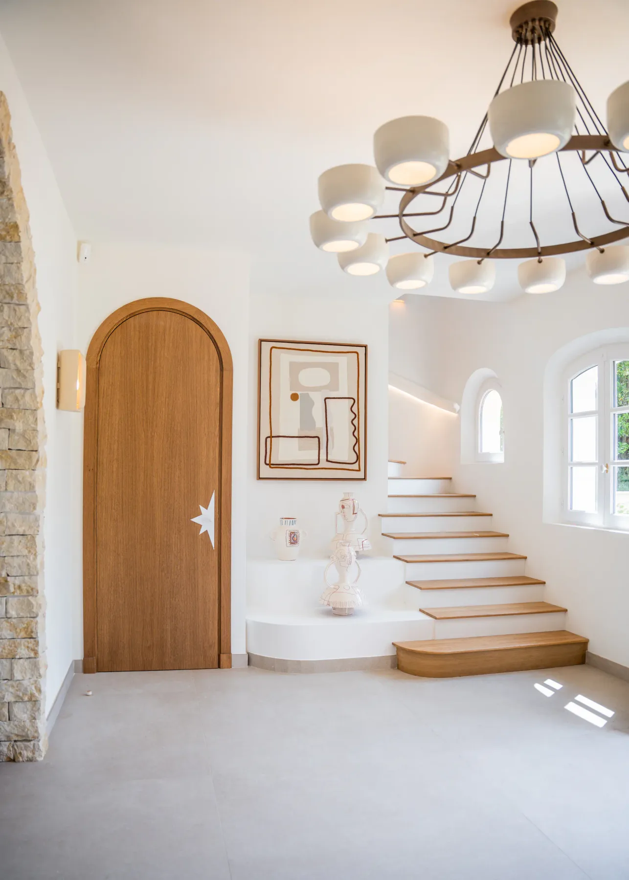 Un interior luminoso muestra una escalera curva junto a una puerta de madera arqueada.