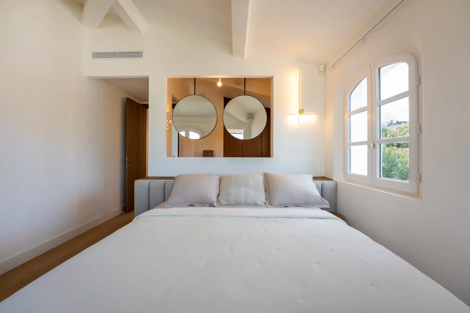 Dormitorio luminoso con cama doble, ventana y dos espejos decorativos redondos.