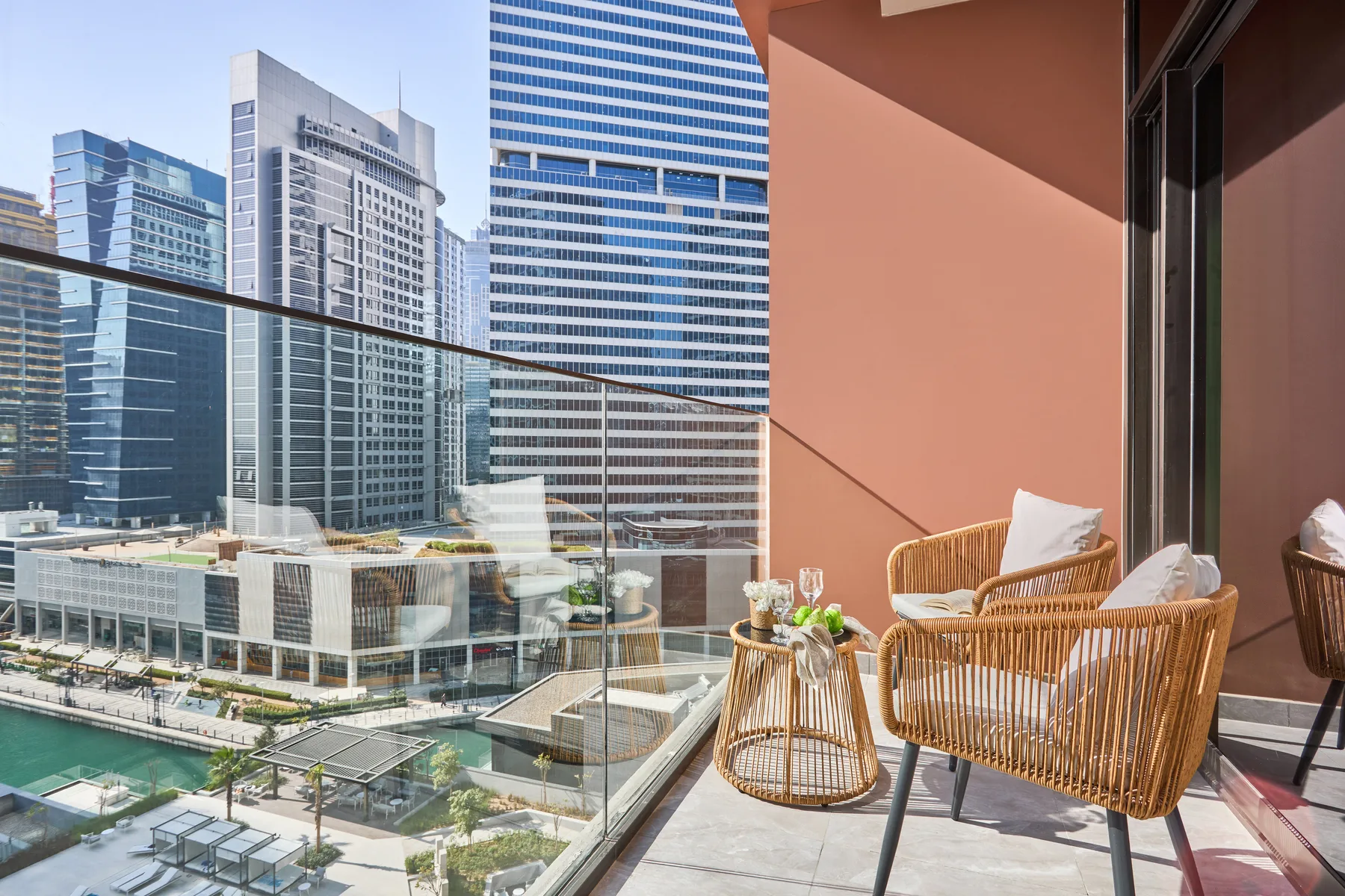 A balcony with outdoor seating overlooks modern buildings and a waterway.