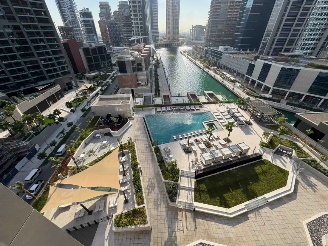 Vista elevada de una terraza con piscina junto a un canal y edificios altos.