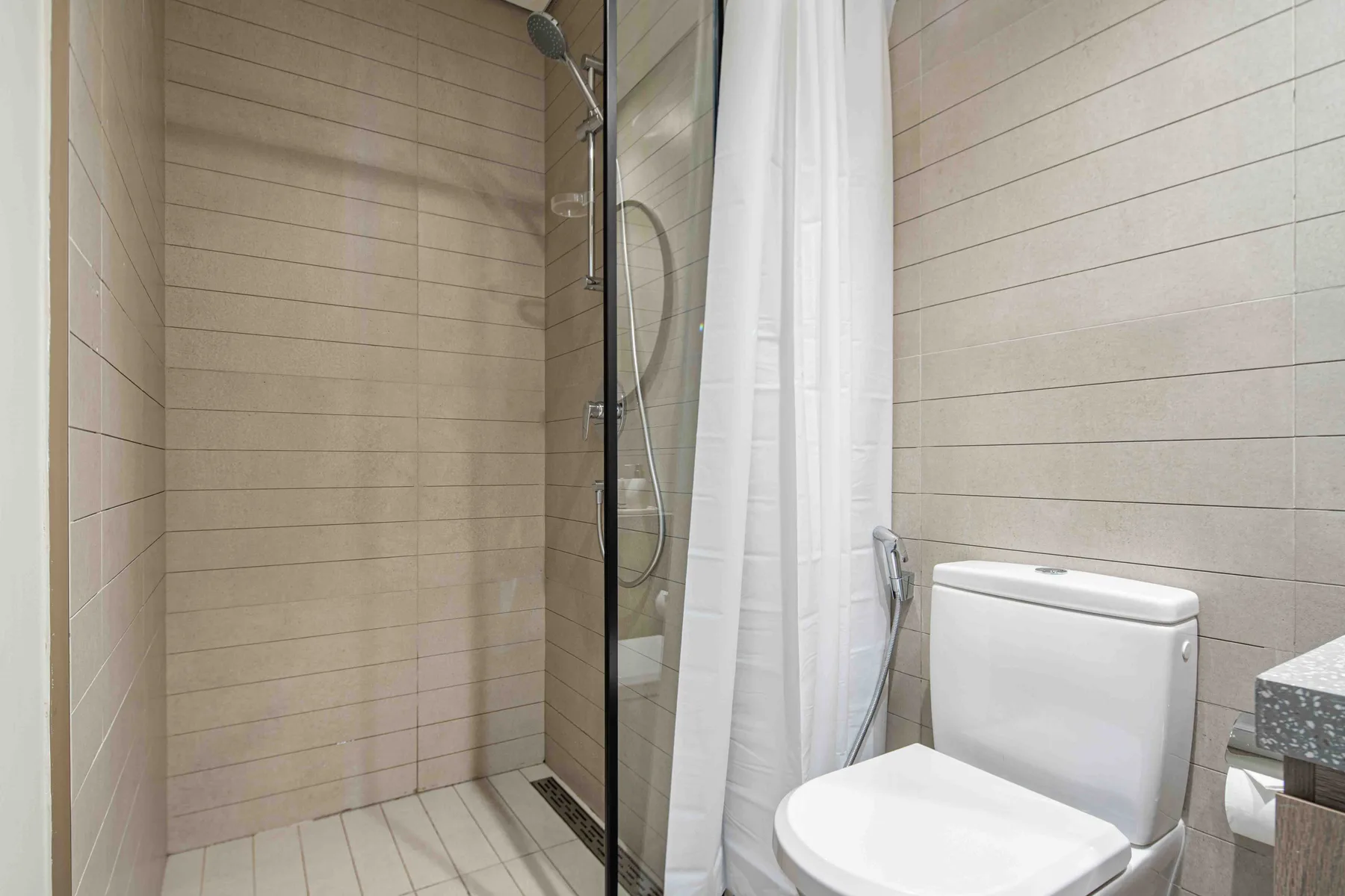 Un baño alicatado con ducha, cortina blanca e inodoro.