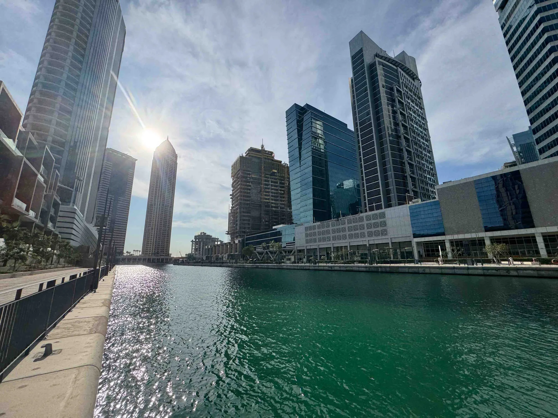 Un canal junto al agua pasa junto a edificios modernos de gran altura bajo un cielo nublado.