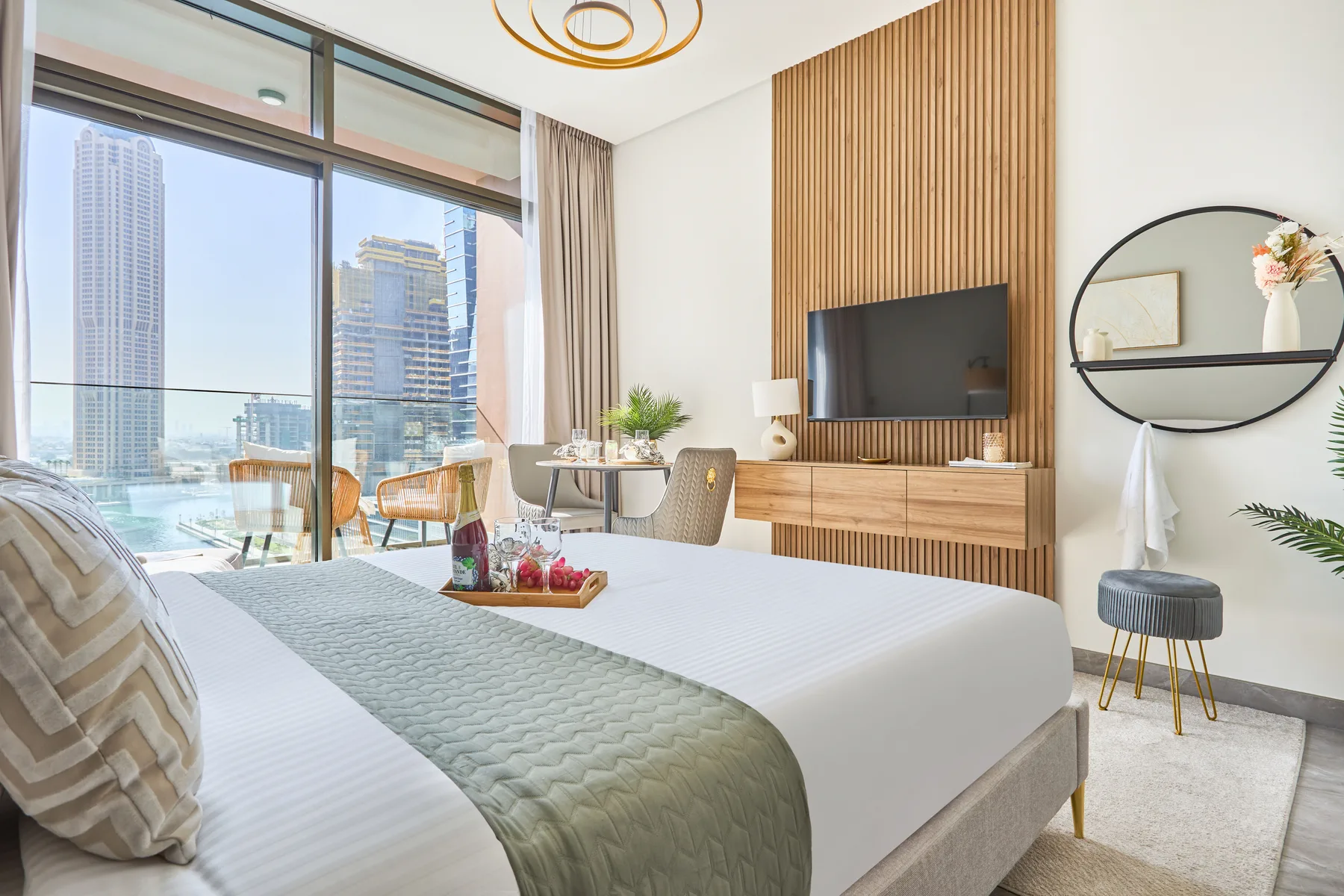 A bright bedroom with a large bed, floor-to-ceiling windows, and a wall-mounted television.