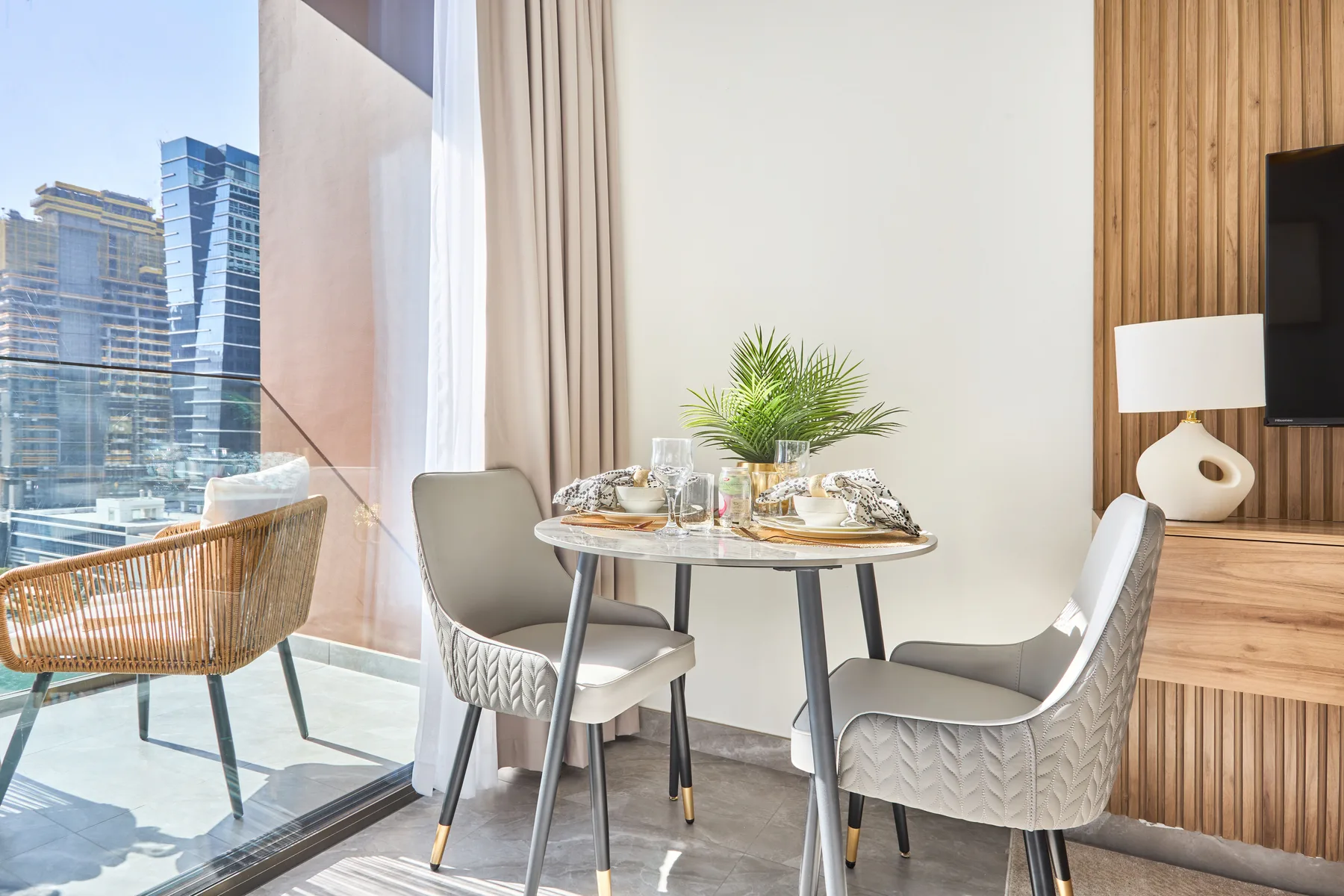 Una mesa de comedor con sillas está junto a una ventana de piso a techo con vista a edificios cercanos.