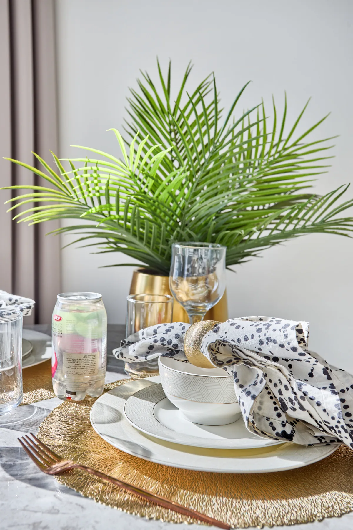 A dining table is set with plates, glassware, and a leafy centerpiece.