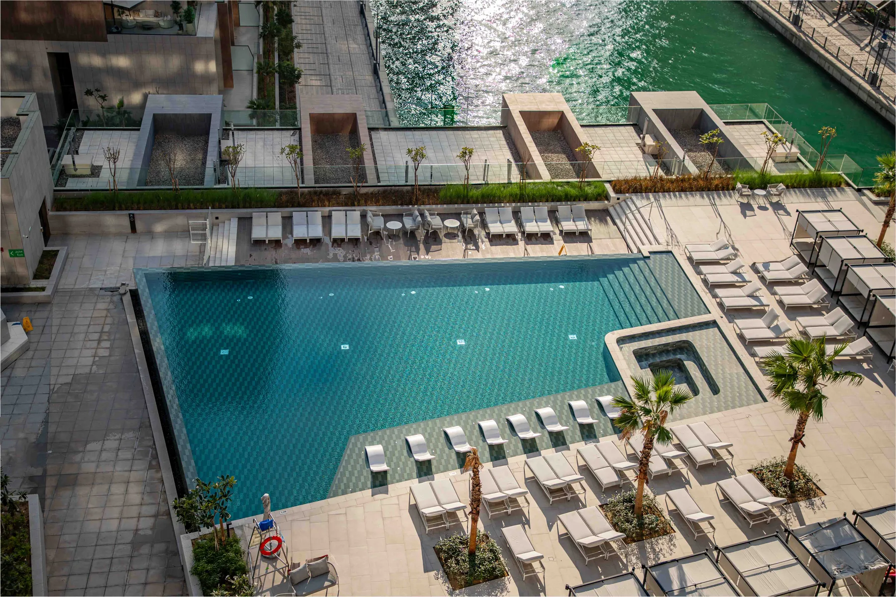 Una piscina al aire libre está rodeada por una terraza pavimentada y asientos de descanso.