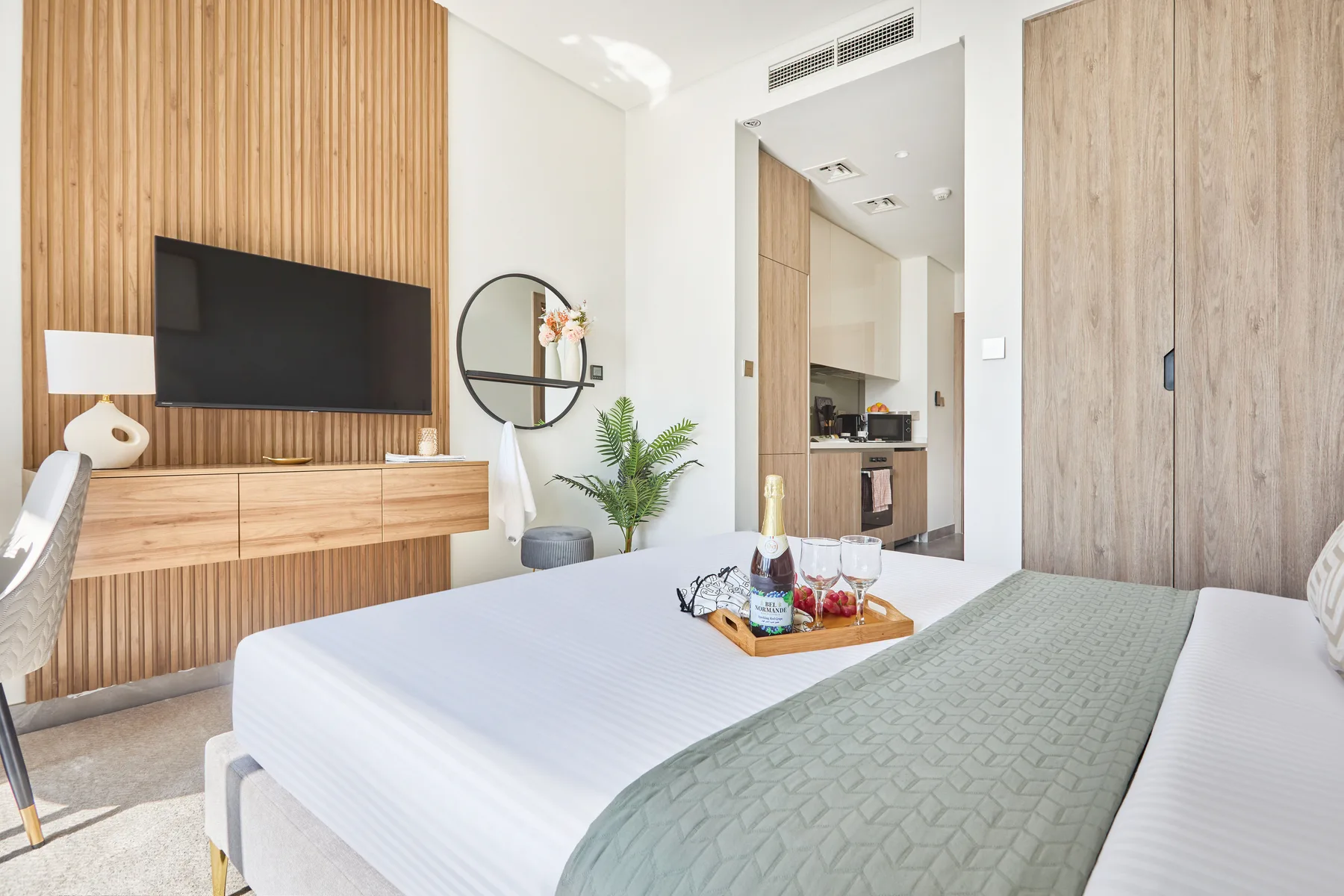 A bright bedroom has a neatly made bed and a television mounted on a wood-paneled wall.