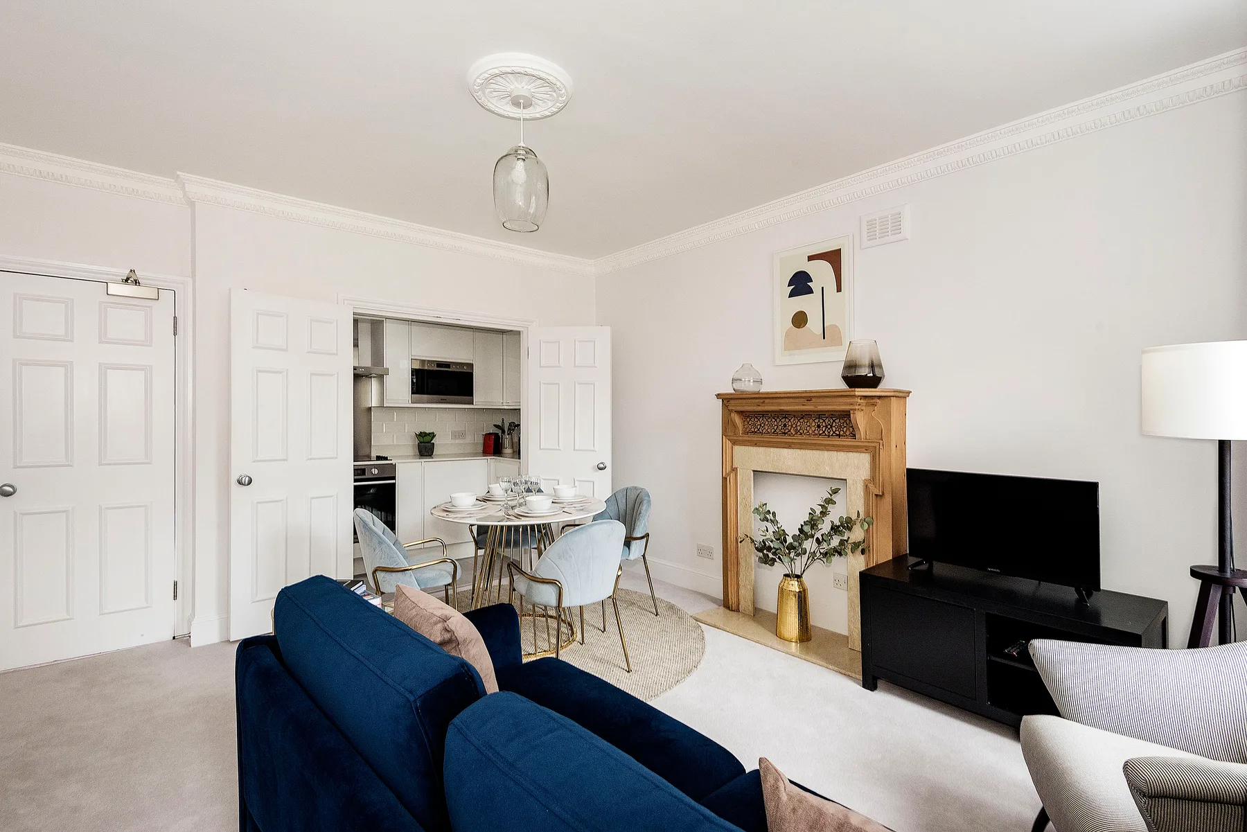 Una sala luminosa con asientos azules, un televisor y un comedor.