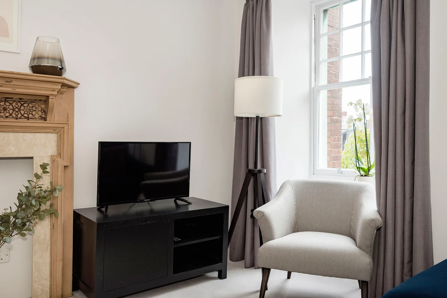 Una zona de estar con televisor, sillón y ventana alta.