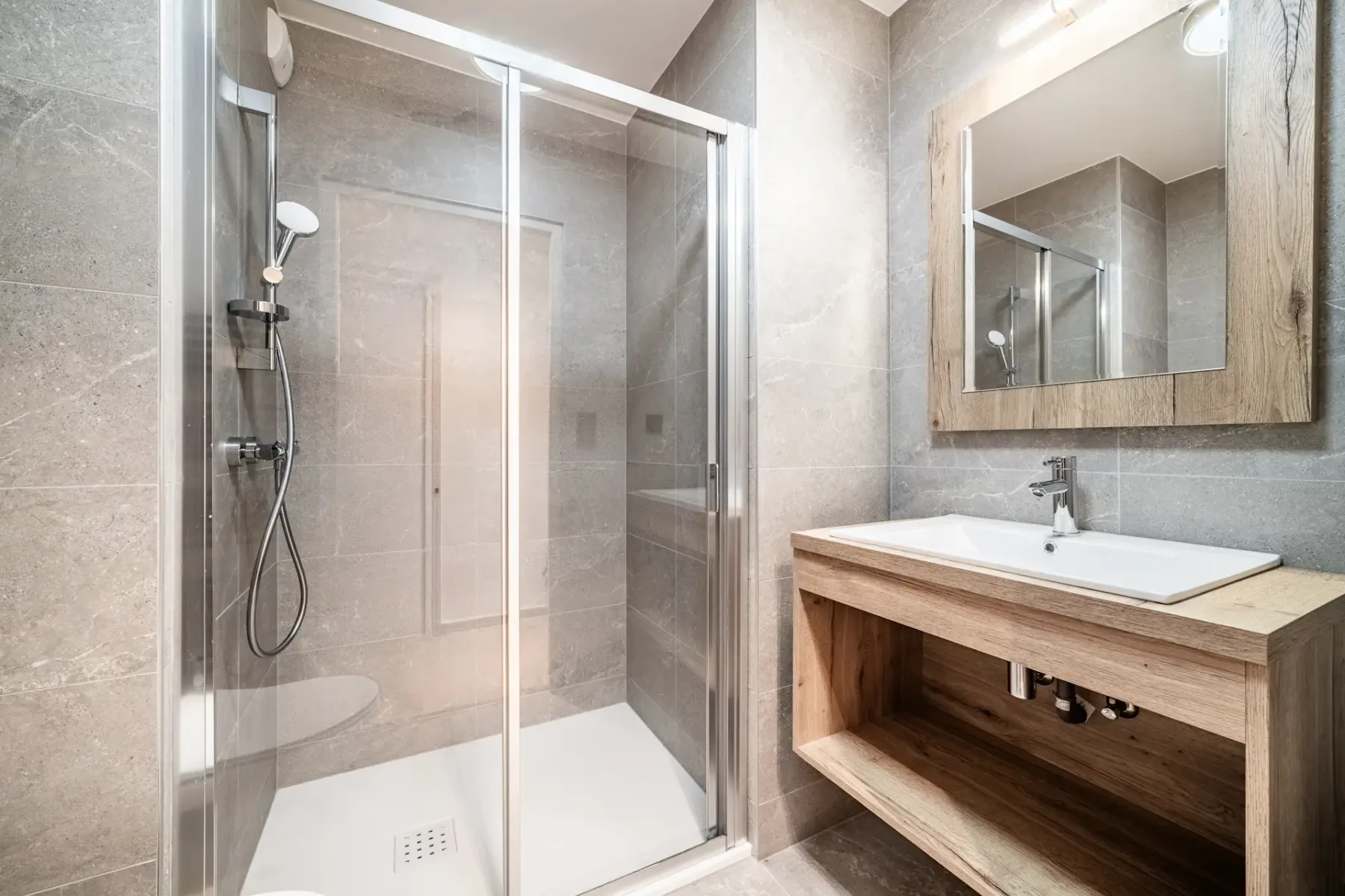 Modern bathroom with a glass-enclosed shower, wall-mounted toilet, gray tile walls, and a wooden countertop.
